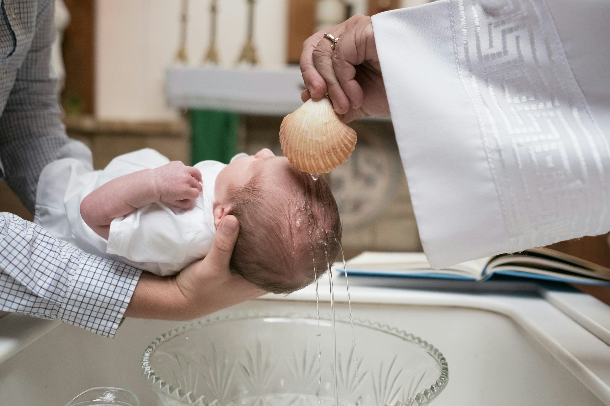 Ksiądz polewa wodą główkę dziecka nad chrzcielnicą